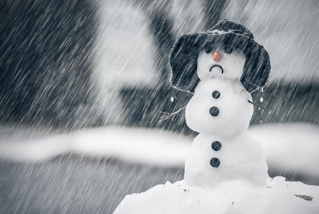 Snowman standing in a snowstorm with a frowny face.
